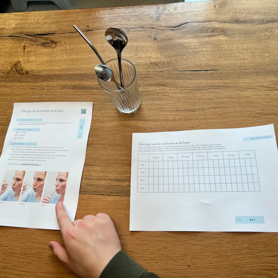 Oefenbladen voor de lippen, met lepels in een glas op de praktijktafel