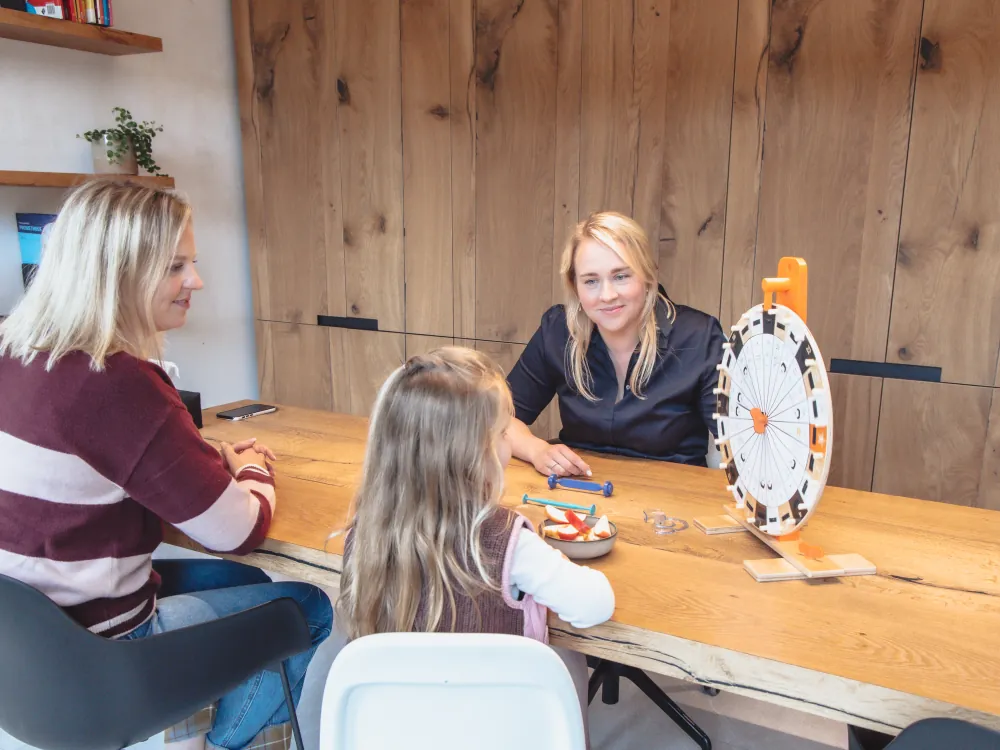 Logopedist, ouder en kind aan tafel met het oefenwiel voor mondoefeningen