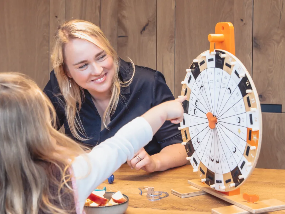 Astrid oefent met een kind aan tafel met een draaiwiel